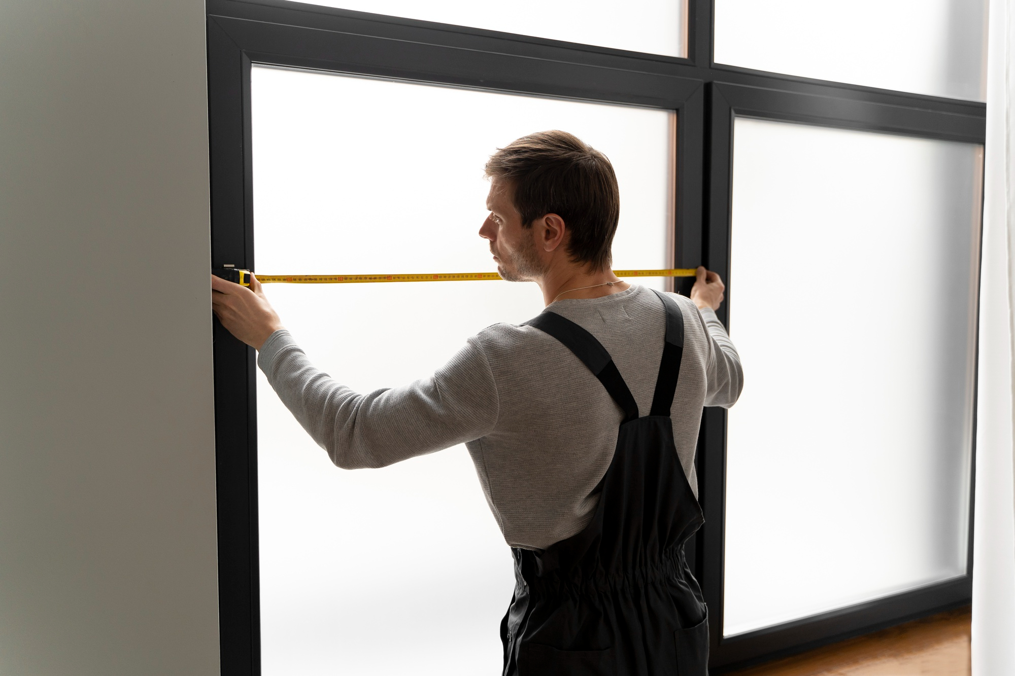 Man measuring a window with a measuring tape, representing mistakes to avoid when installing blinds