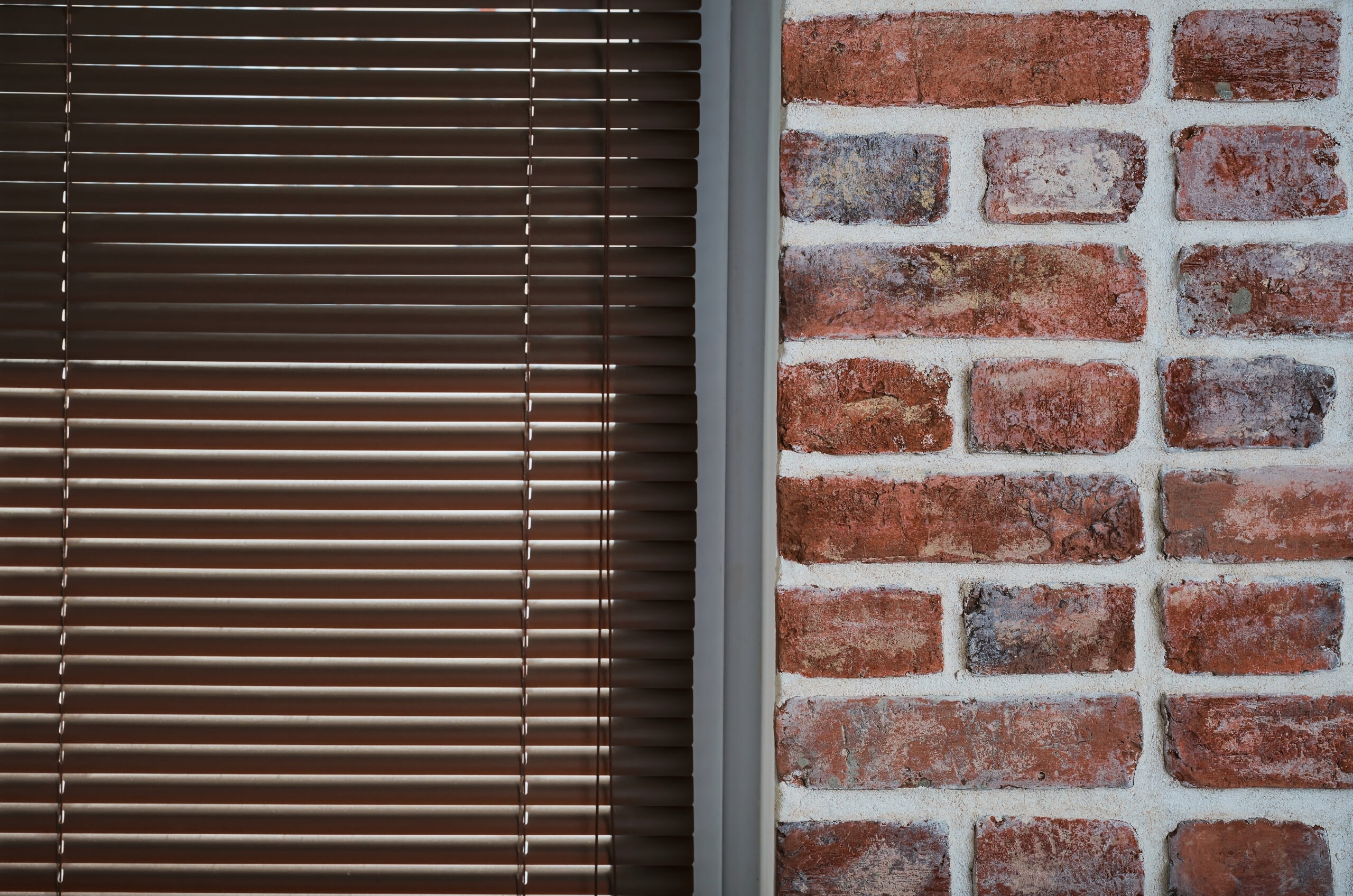 Brick faced wall, with a window with brown venetian blinds, representing made to measure blinds